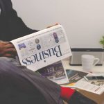 Businessman reading a financial newspaper at a desk, highlighting finance and commerce theme.